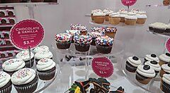 Esposizione di cupcake assortiti in una pasticceria, con etichette dei prezzi.