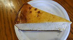 Fetta di cheesecake su un piatto di carta, con tavolo di legno.
