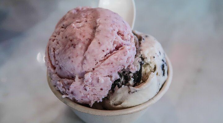 Coppetta di gelato con due gusti, uno rosa e uno con pezzi di biscotto, su tavolo di marmo.