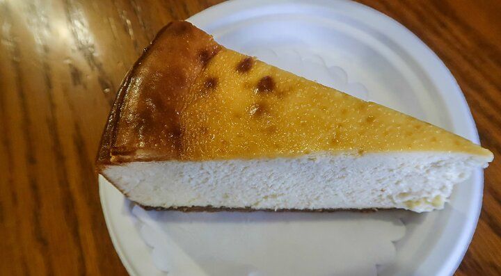 Fetta di cheesecake su un piatto di carta, con tavolo di legno.
