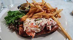 Lobster roll con patatine fritte e insalata su un piatto bianco.