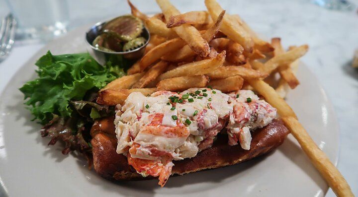 Lobster roll con patatine fritte e insalata su un piatto bianco.