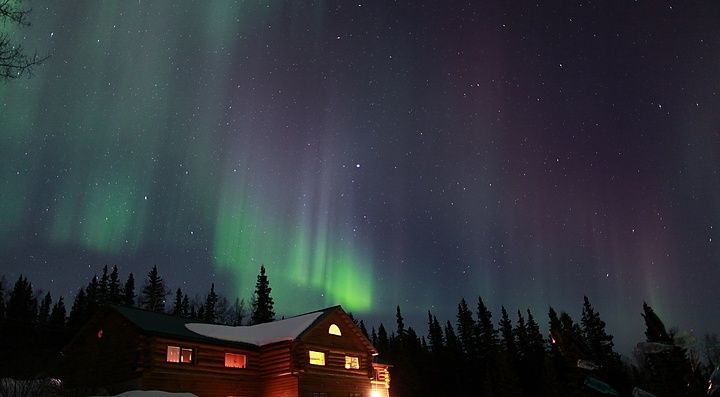 Aurora boreale in Alaska, sopra una casa in mezzo ai boschi.