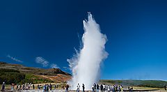Geyser in eruzione sotto un cielo azzurro con turisti intorno.