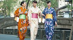 Tre persone in kimono colorati camminano su un ponte di pietra.