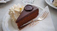 Fetta di Sachertorte austriaca con panna su un piatto.