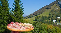 Piatto di salumi e formaggi tipici del Trentino con sfondo montano.
