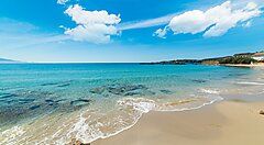 Spiaggia di Alghero con mare azzurro e cielo sereno.