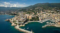 Veduta aerea di una città costiera in Corsica con porticciolo e montagne sullo sfondo.