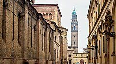 Strada con edifici storici e campanile nel centro di Parma.