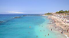 Spiaggia turistica a Tenerife con persone che nuotano nell'acqua limpida.