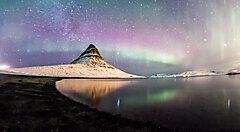 Aurora boreale sopra un paesaggio montuoso riflesso in un lago.