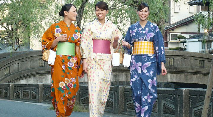 Tre persone in kimono colorati camminano su un ponte di pietra.