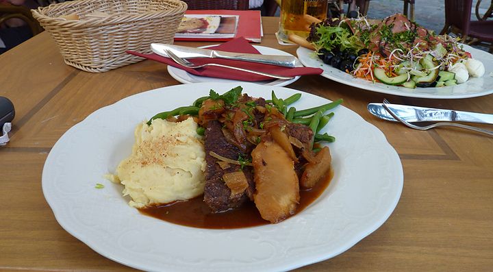 Piatto di manzo brasato con purè di patate e contorni su tavola in legno.