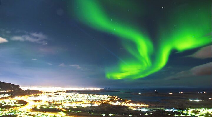 Aurora boreale verde nel cielo notturno sopra una città illuminata.