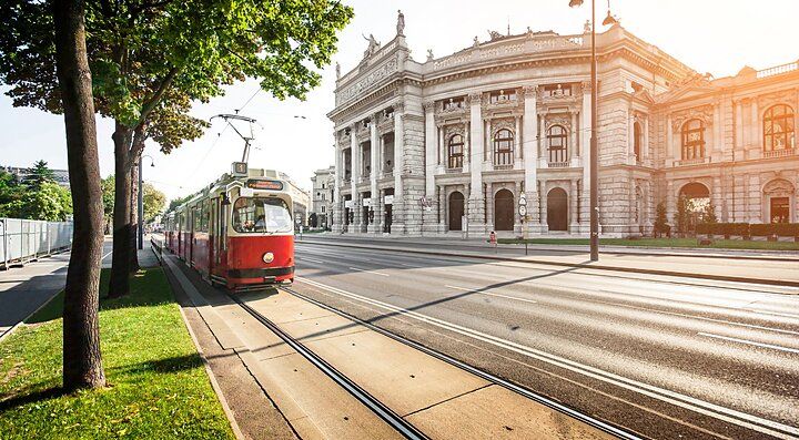 Tram rosso davanti al Burgtheater di Vienna su una strada soleggiata.