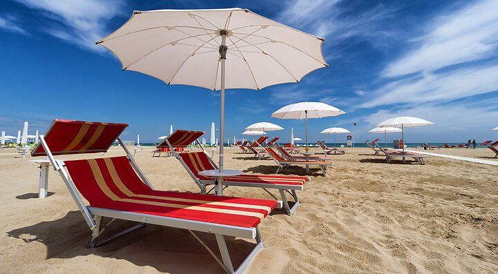 Spiaggia sabbiosa di Rimini con lettini e ombrelloni sotto un cielo blu.