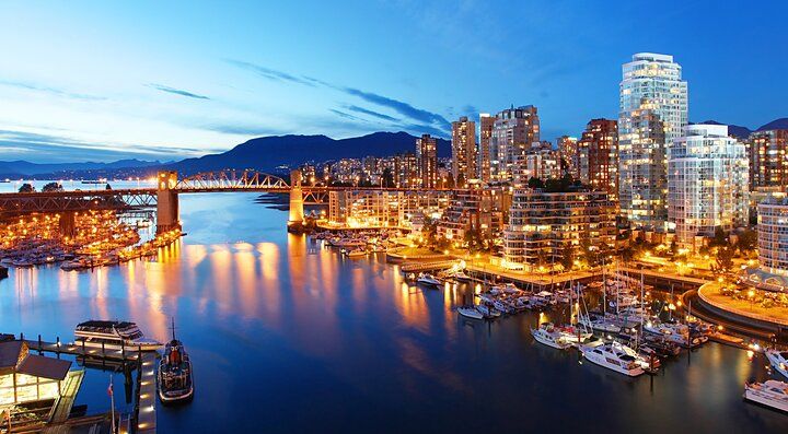 Skyline notturno di Vancouver con edifici illuminati e acqua.