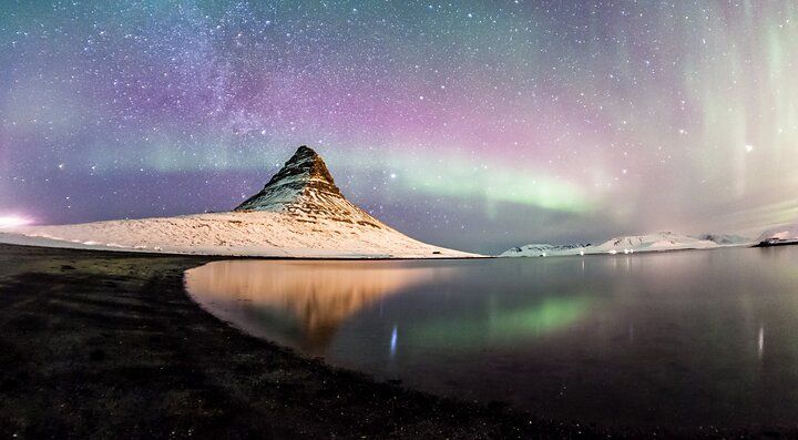 Aurora boreale sopra un paesaggio montuoso riflesso in un lago.