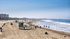 Spiaggia affollata in California con torrette di salvataggio e bagnanti.