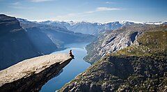 Persona seduta su una scogliera con vista sul fiordo in Norvegia.