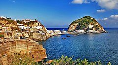 Vista panoramica del porto di Ischia con mare cristallino e colline verdeggianti.