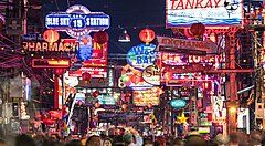 Strada affollata di Pattaya con luci al neon e insegne.