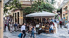 Caffè all'aperto affollato ad Atene con persone che passeggiano.