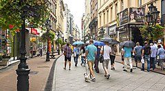 Strada affollata nel centro di Budapest con persone che camminano sotto la pioggia.