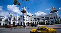Edificio storico a Kuala Lumpur con taxi giallo in primo piano.
