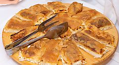 Strudel salato croato servito su un piatto di legno con pinze.