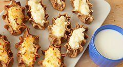 Pasticcini finlandesi con ripieno cremoso su un piatto, accanto a una tazza blu di bevanda bianca.