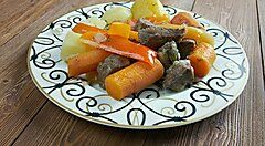 Piatto tradizionale mongolo con carne e verdure colorate su un tavolo di legno.