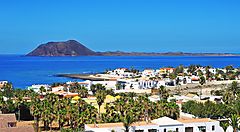 Vista panoramica di un villaggio costiero a Fuerteventura con l'oceano e un'isola sullo sfondo.