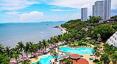 Vista sulla spiaggia e piscina di un resort a Pattaya, con palme e mare sullo sfondo.