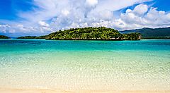 La spiaggia di Ishigaki con acque cristalline e un'isola verde all'orizzonte.