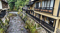 Edifici tradizionali lungo un fiume a Kurokawa Onsen, immersi nella natura.