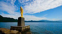 Statua dorata sul Lago Tazawa con montagne sullo sfondo.