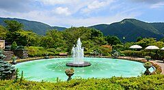 Fontana circondata da verde al Parco Gora, con montagne sullo sfondo.