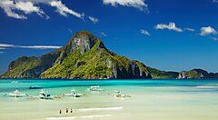 Spiaggia tropicale delle Filippine con montagne e barche sull'acqua.