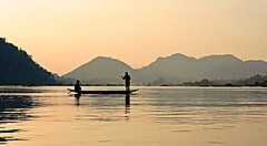 Pescatori su una barca al tramonto in un fiume in Laos.