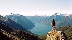Escursionista su un promontorio con vista su montagne e lago in Nuova Zelanda.