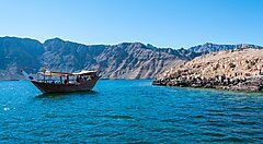Barca tradizionale su acque blu con montagne sullo sfondo in Oman.