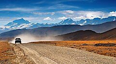 Auto su strada sterrata con montagne del Tibet sullo sfondo.