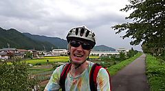 Ciclista su un sentiero rurale a Satoyama circondato da campi e montagne.