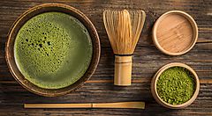 Tè matcha giapponese con accessori tradizionali su tavola di legno.