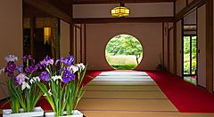 Interno del tempio Meigetsuin con tatami e fiori davanti a una finestra circolare.