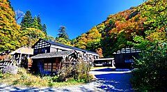 Edifici tradizionali circondati da colline boscose a Tsurunoyu Onsen in autunno.