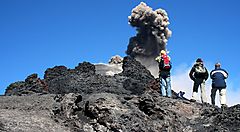 Escursionisti osservano un'eruzione sull'Etna con cielo azzurro.