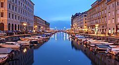 Canal Grande a Trieste al tramonto con barche e palazzi illuminati.